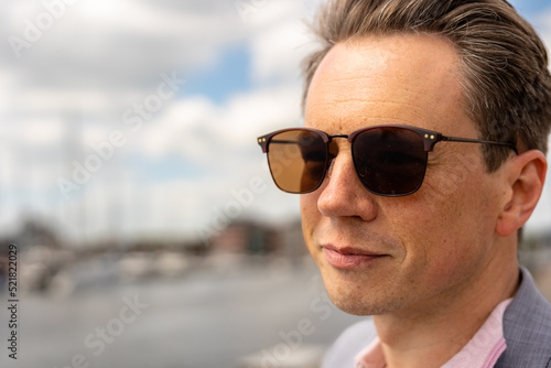 Close up portrait of a handsome businessman in a casual grey suit in front of a busy marina with luxury yachts moored up