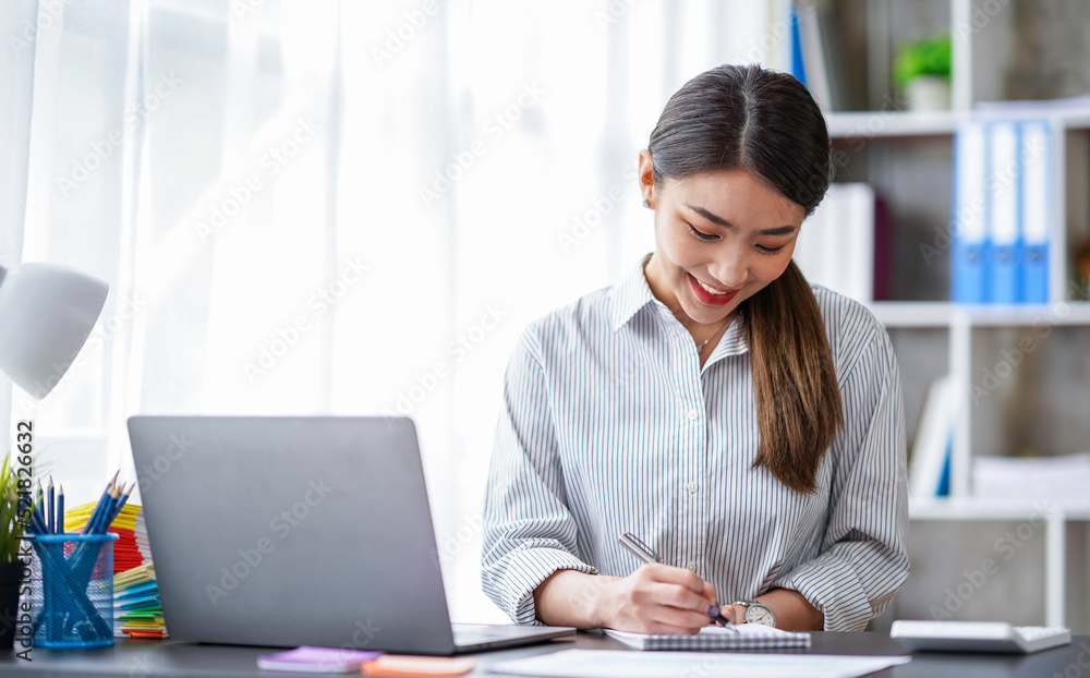 Confident successful businesswoman, freelancer or employee, sits at her work desk at home or in the office, uses a laptop, chats with colleagues, responds to emails, browses the Internet