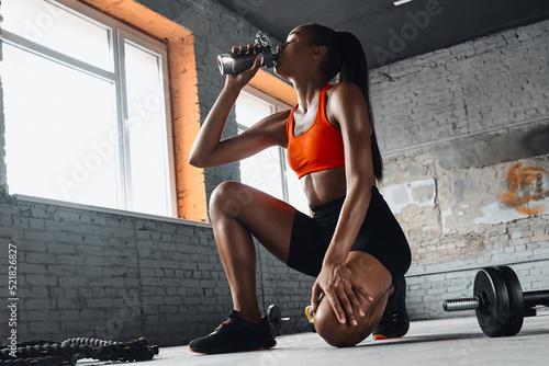 Tablou pe pânză Young African woman drinking water while taking a break in gym