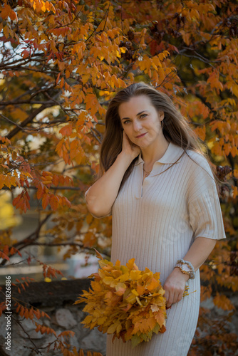Portrait of beautiful woman in white dress holding bouquet with autumn leaves.