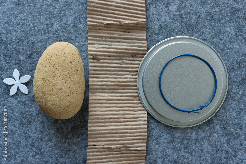 paper flower, rounded stone (worn brick), corrugated cardboard, metal disc, and loop earring on gray felt paper flower, rounded stone (worn brick), corrugated cardboard, metal disc, and loop earring on gray felt