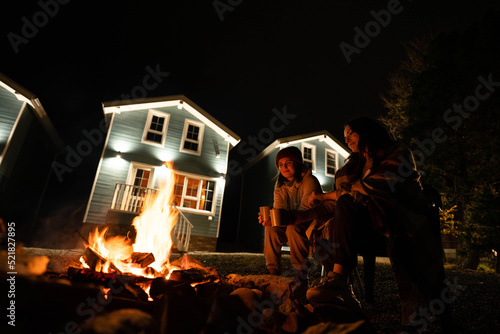 Two women sit by the fire at night. Backyard of a wooden house.