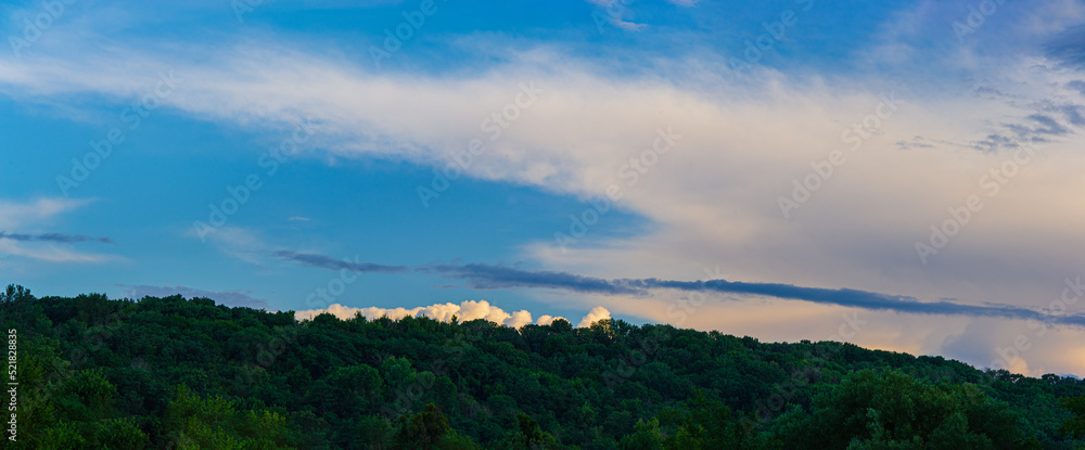 White cloud on top of a hill covered with deciduous forest.