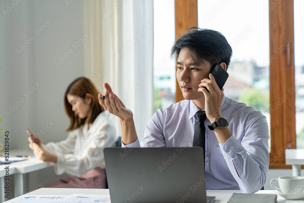 Asian businessman talking on the phone in a serious mood in the office Asian businessman talking on the phone in a serious mood in the office