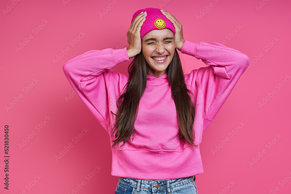 Surprised young woman in hooded shirt holding head in hands against pink background Surprised young woman in hooded shirt holding head in hands against pink background