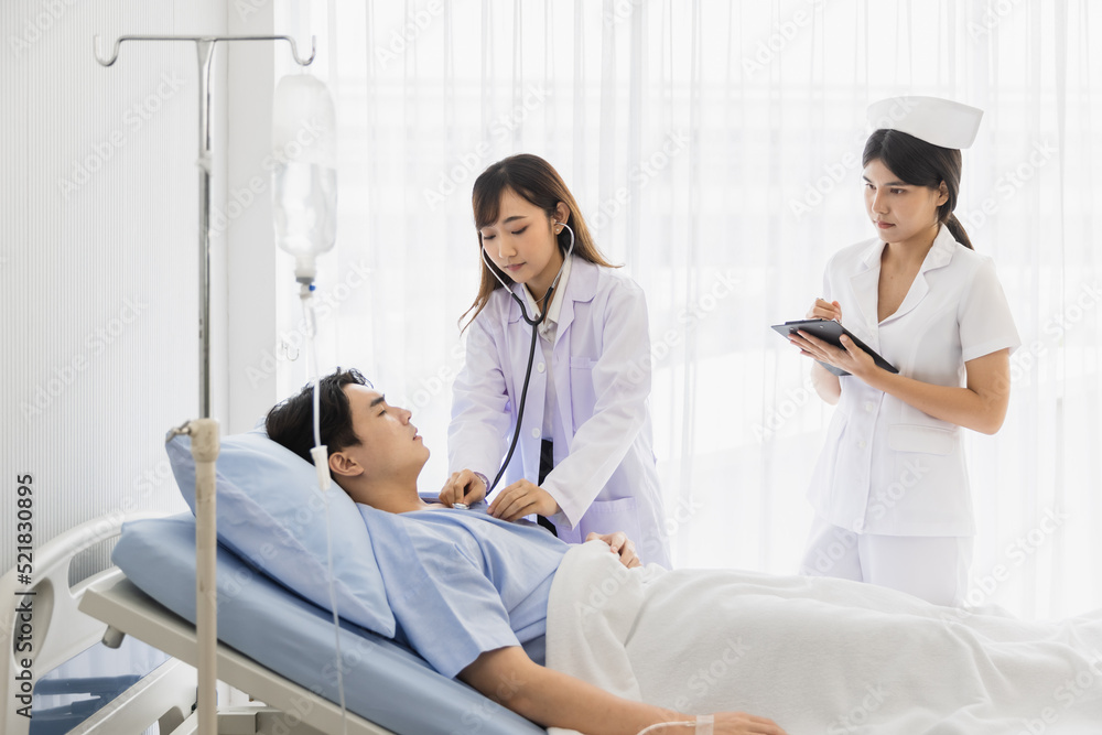 Female doctor and nurse visiting and using stethoscope checking examine heartbeat male patient at hospital Female doctor and nurse visiting and using stethoscope checking examine heartbeat male patient at hospital