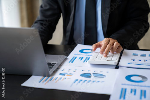 Asian male finance staff is calculating by using a calculator. Investment results to report to his boss at the meeting. On the table in the office, the concept of calculating investment results