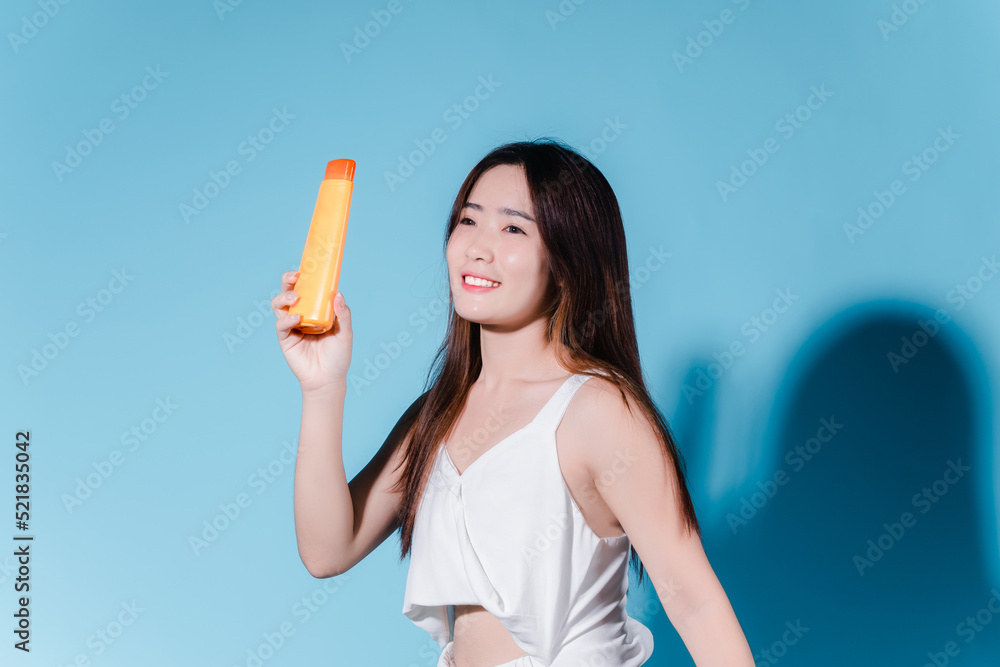 Charming asian beauty woman hold sun cream with sun protection uv or sunscreen on the blue background Charming asian beauty woman hold sun cream with sun protection uv or sunscreen on the blue background