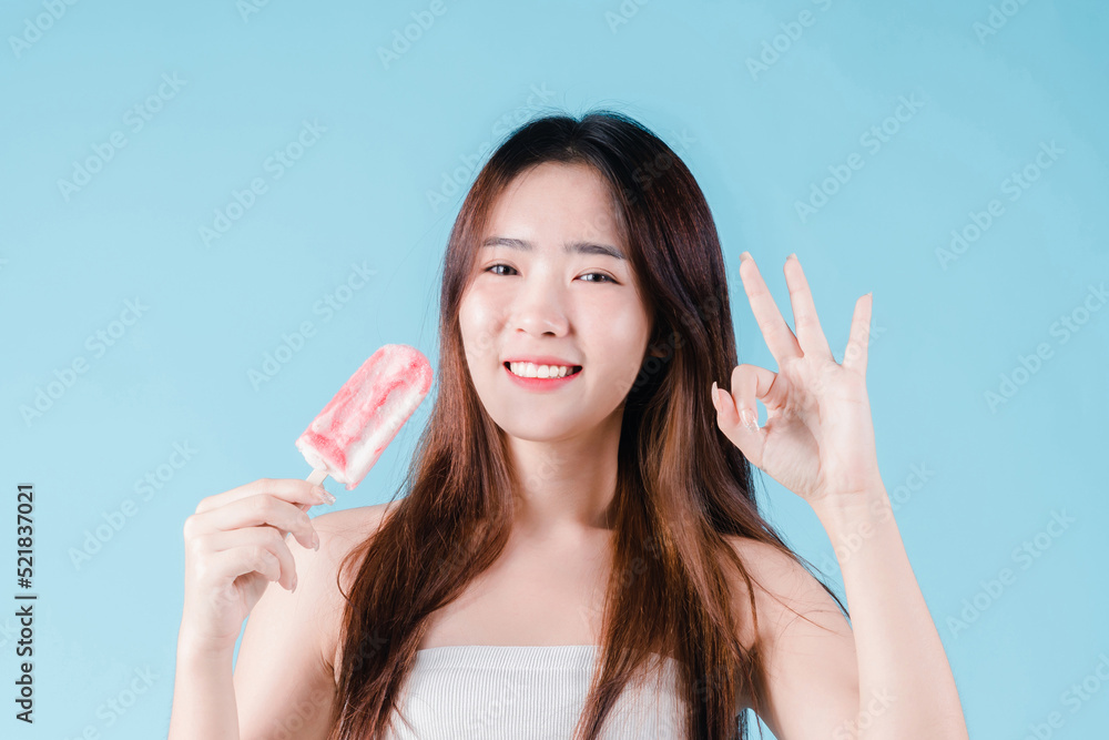 Asian woman hold popsicle and show ok gesture have strong teeth on the blue background Asian woman hold popsicle and show ok gesture have strong teeth on the blue background