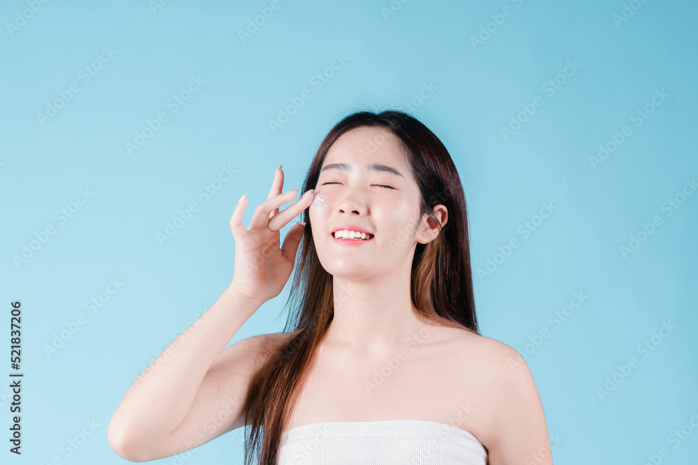 Asian beauty woman applying moisturizer, lotion, serum on facial by skin care on the blue background Asian beauty woman applying moisturizer, lotion, serum on facial by skin care on the blue background