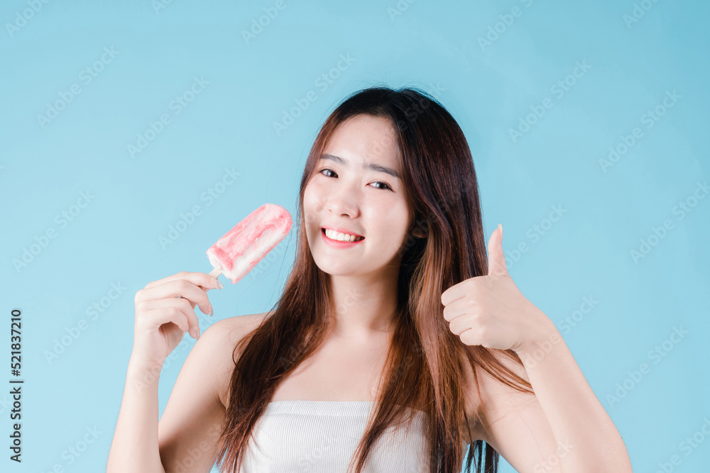Asian woman hold popsicle and show ok gesture have strong teeth on the blue background Asian woman hold popsicle and show ok gesture have strong teeth on the blue background