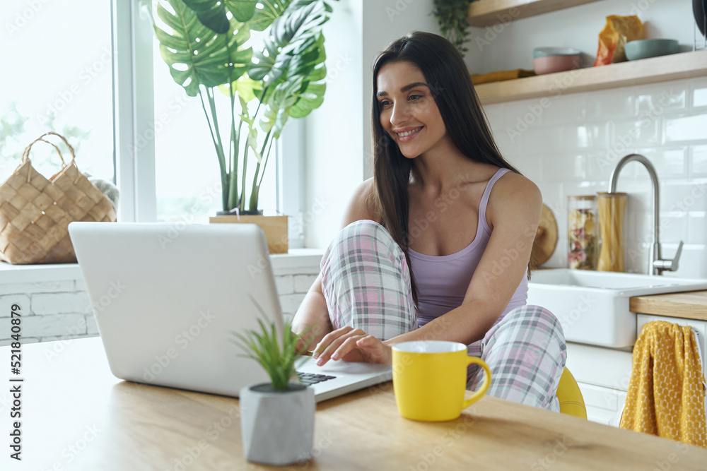Beautiful woman using laptop while sitting at the kitchen counter at home