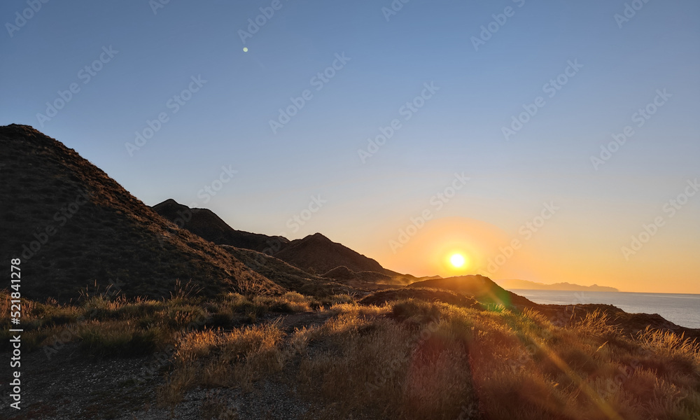 sunrise over the mountains at the coast of almeria, andalusia with sunbeams and seemingly the moon above