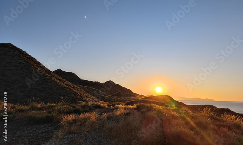 sunrise over the mountains at the coast of almeria  andalusia with sunbeams and seemingly the moon above