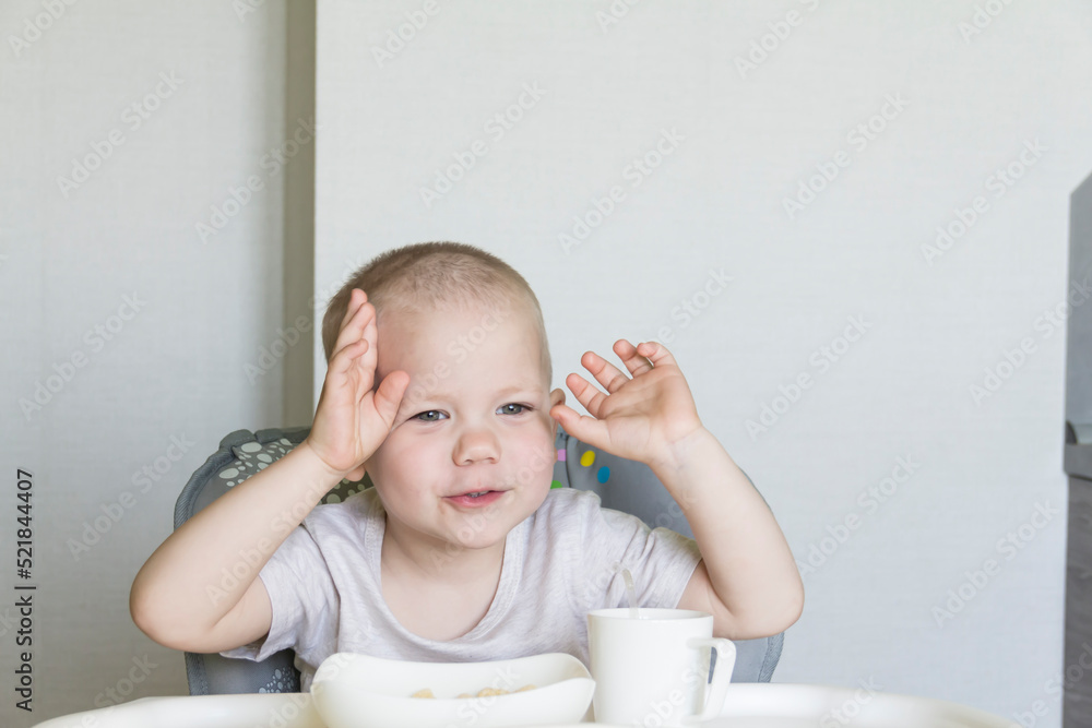 A little boy with a short haircut independently and appetitiously eats food and drinks juice from a tube in a child's chair. A little boy with a short haircut independently and appetitiously eats food and drinks juice from a tube in a child's chair.