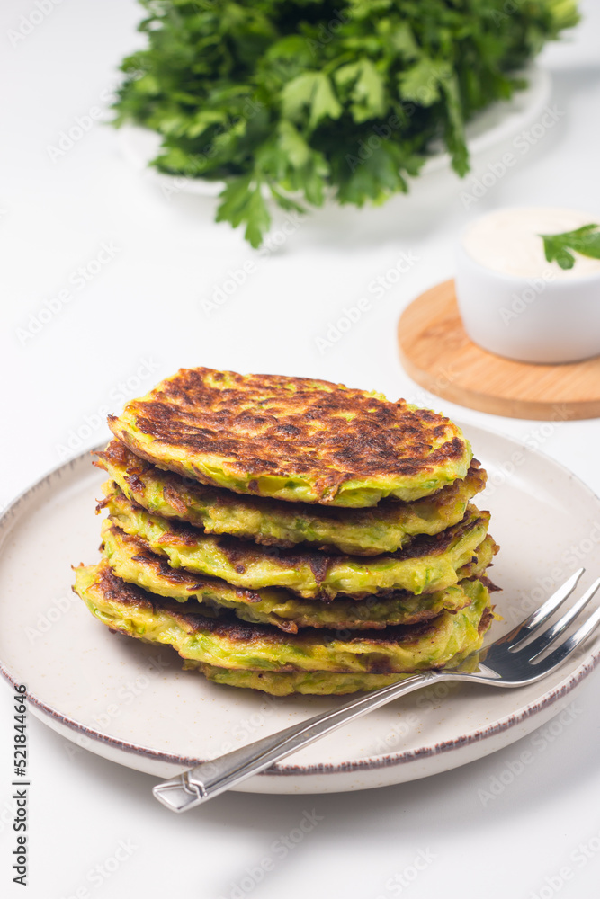 Vegetarian zucchini fritters or courgettes pancakes, served with fresh herbs and sour cream.