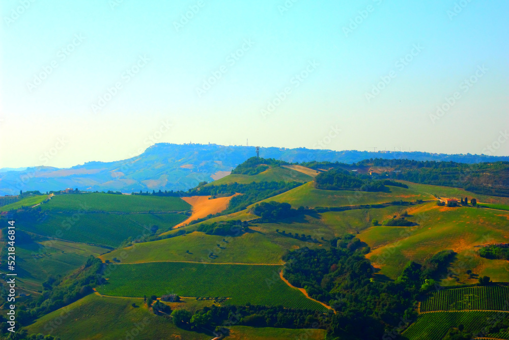 Enchanting panorama in Acquaviva Picena with deep green meadows sitting on the sweet and gentle hills typical of Marche landscapes with technological towers in the background on a summer day
