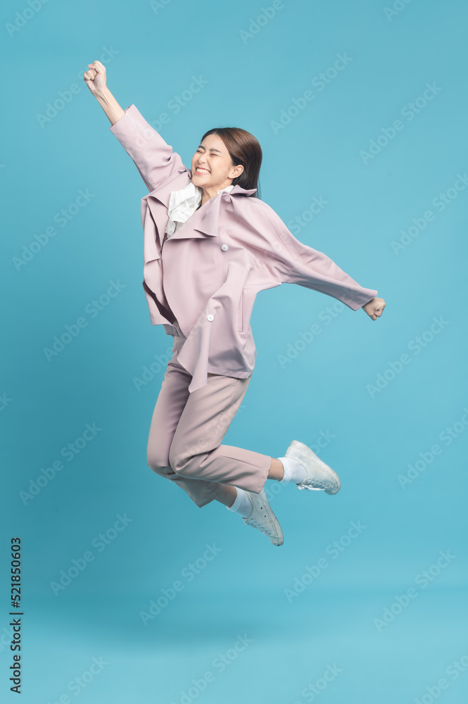 Young beautiful asian woman with smart casual cloth wearing pink coat jumping with excite feeling isolated on blue background Young beautiful asian woman with smart casual cloth wearing pink coat jumping with excite feeling isolated on blue background