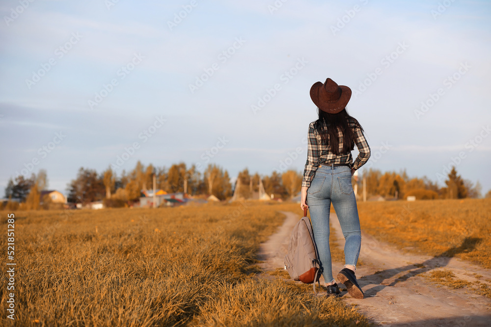 A young girl is traveling around the city hitchhiking. A beautiful young girl went on vacation. A female student in a cowboy hat on the road in autumn.