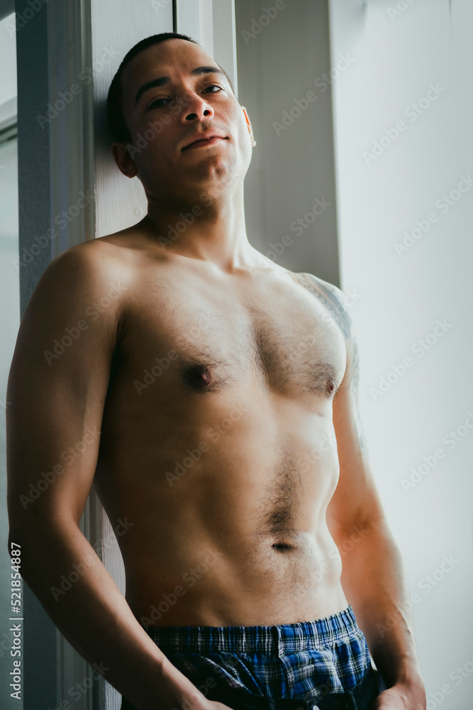 Fototapeta premium Latino male veteran posing in door frame, looking down at the camera while shirtless