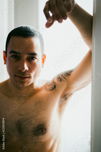 Latino male veteran posing in door frame looking at the camera while shirtless