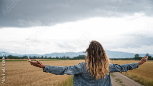 Young woman standing in beautiful nature of wheat fields with her arms spread widely