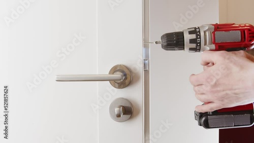 
Door lock repair. The man drives the screw in the door with a drill.