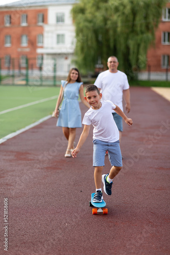 A boy learns to skate, his parents look at him from behind