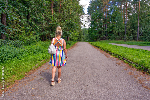A girl walks down the road in the woods in a dress