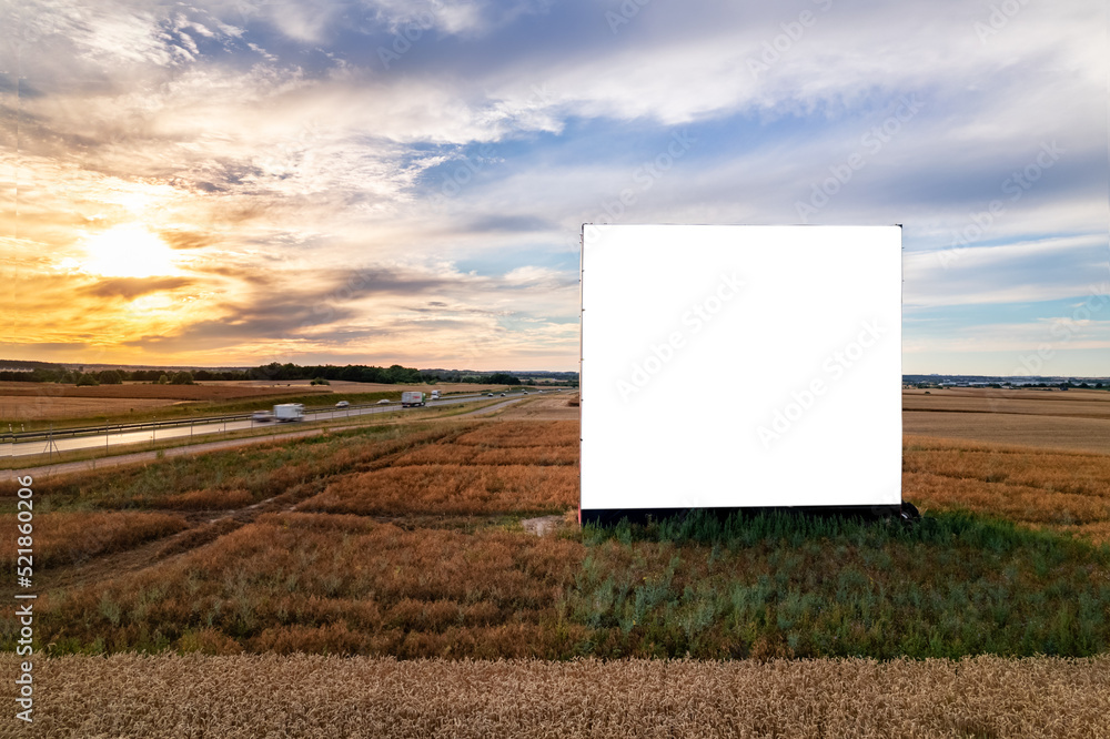 Aerial drone shot of big blank billboard near busy highway or motorway at sunset