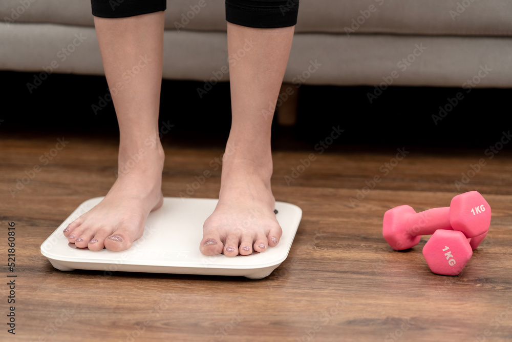 Sporty woman is standing on electronic the scales to weigh and checking results after diet and losing Sporty woman is standing on electronic the scales to weigh and checking results after diet and losing