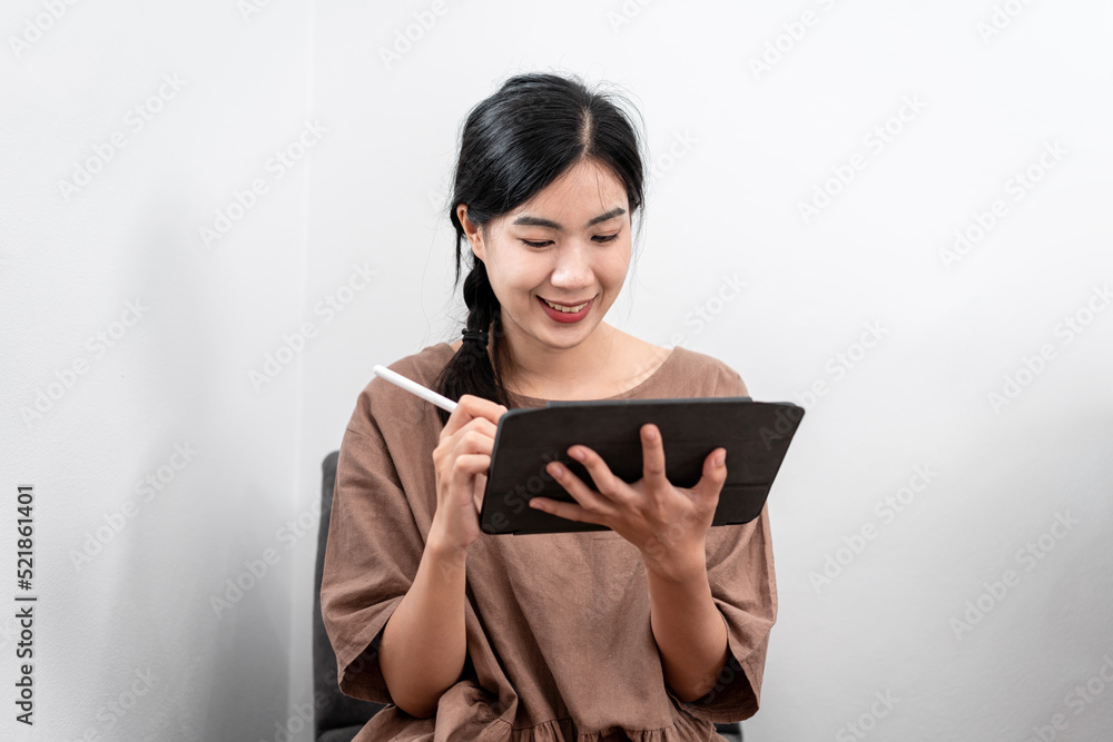 Beautiful woman is writing notes and work schedule in tablet while sitting to relaxation on carpet