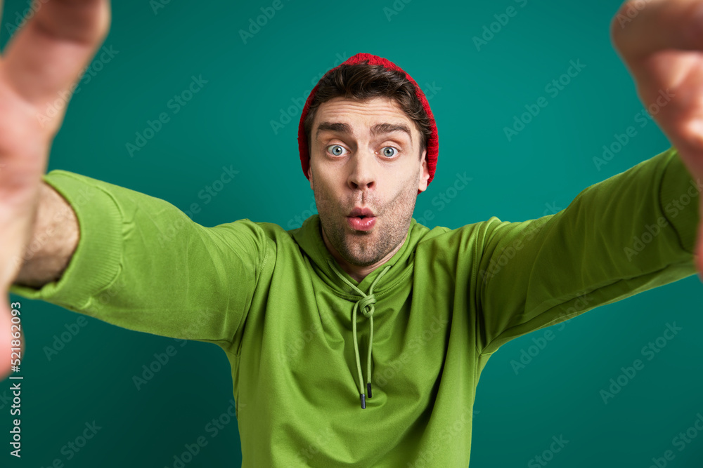 Surprised young man looking through a finger frame while standing against green background Surprised young man looking through a finger frame while standing against green background