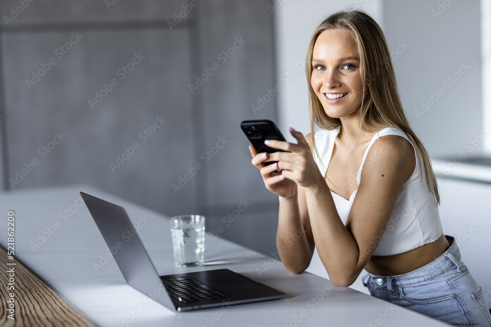 Young woman checks social media from mobile phone at kitchen Young woman checks social media from mobile phone at kitchen