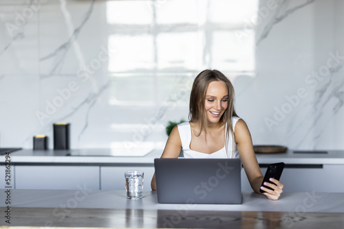 Work at home. Young woman use a laptop to work in the kitchen use phone © F8  \ Suport Ukraine