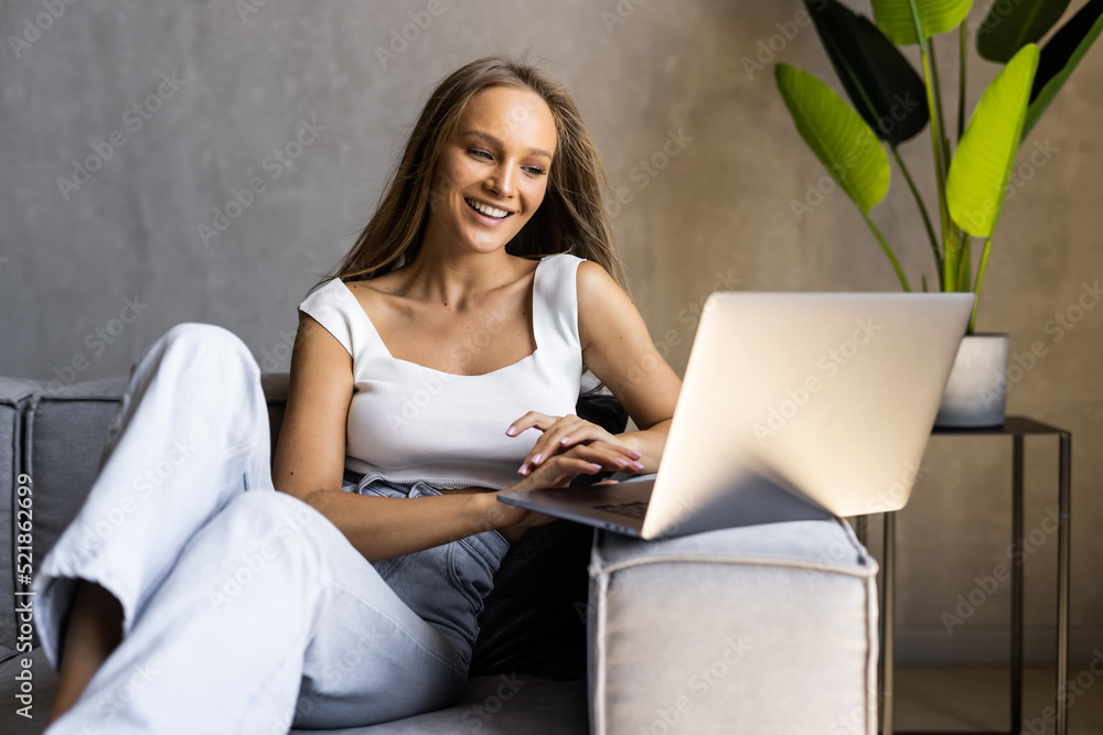 Cheerful young lady holding laptop while laying on couch. Young woman relaxing after work, using internet connection Cheerful young lady holding laptop while laying on couch. Young woman relaxing after work, using internet connection