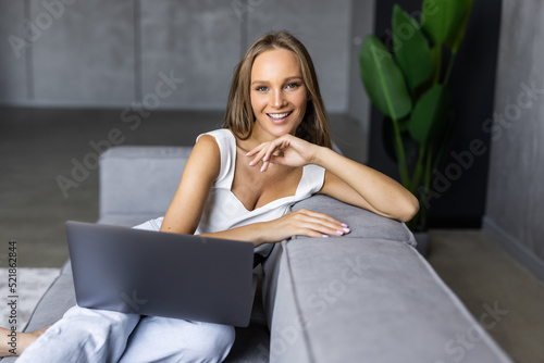 Young woman using laptop while sitting on comfortable sofa at home