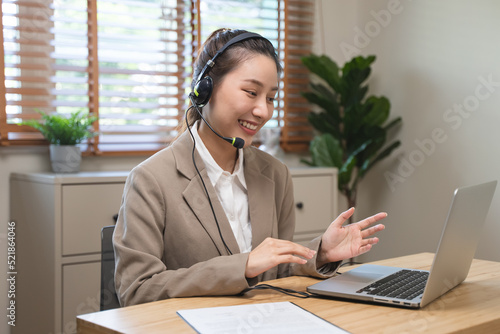 Happy young asian business woman waving hands to greeting partner during making video conference with her team.