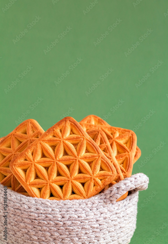 Square biscuits close up in a white crochet basket on a green background. Copy space.