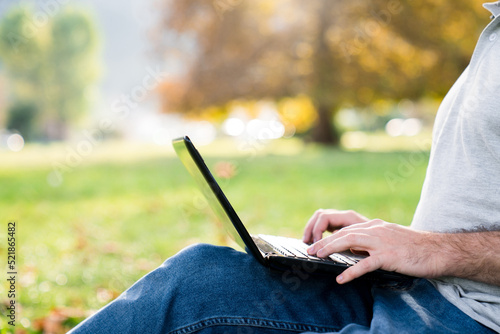 Freelancer workplace with laptop in autumn park. Digital nomad working in traveling from outdoor office at nature. Man in workation. Student in online education. Close up of male hands