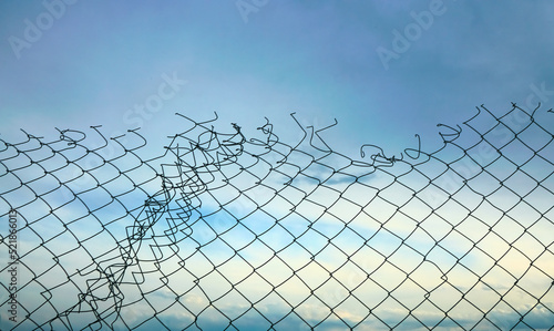 Canvas Print Opening in metallic fence against a blue sky with white clouds