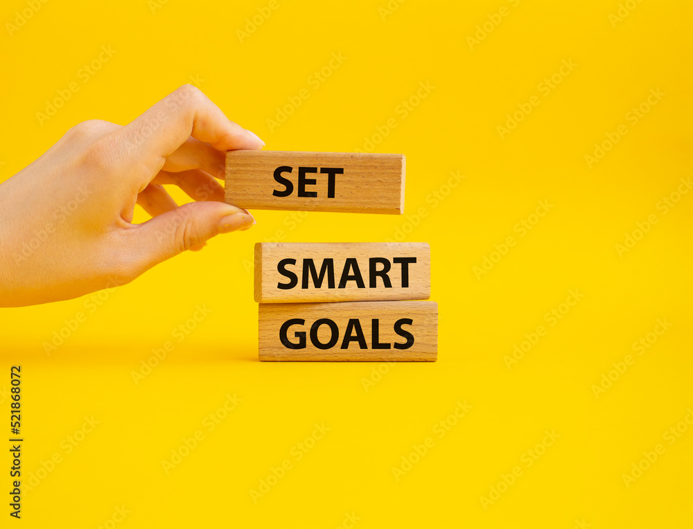 Naklejka premium Set smart goals symbol. Concept words Set smart goals on wooden blocks. Beautiful yellow background. Businessman hand. Business and Set smart goals concept. Copy space.