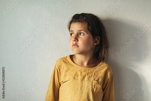 Fotografia Sad pensive girl child in a yellow blouse looks seriously out the window during