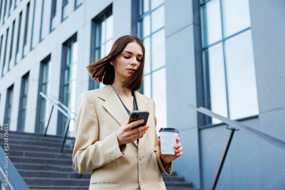 A young brunette girl against the backdrop of a business center, office center. On the go, he reads the news from his smartphone. A young brunette girl against the backdrop of a business center, office center. On the go, he reads the news from his smartphone.
