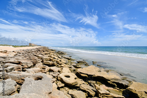 Coquina rocks line the beach with blue skies above in Palm Coast, Florida between St Augustine and Flagler Beach. 