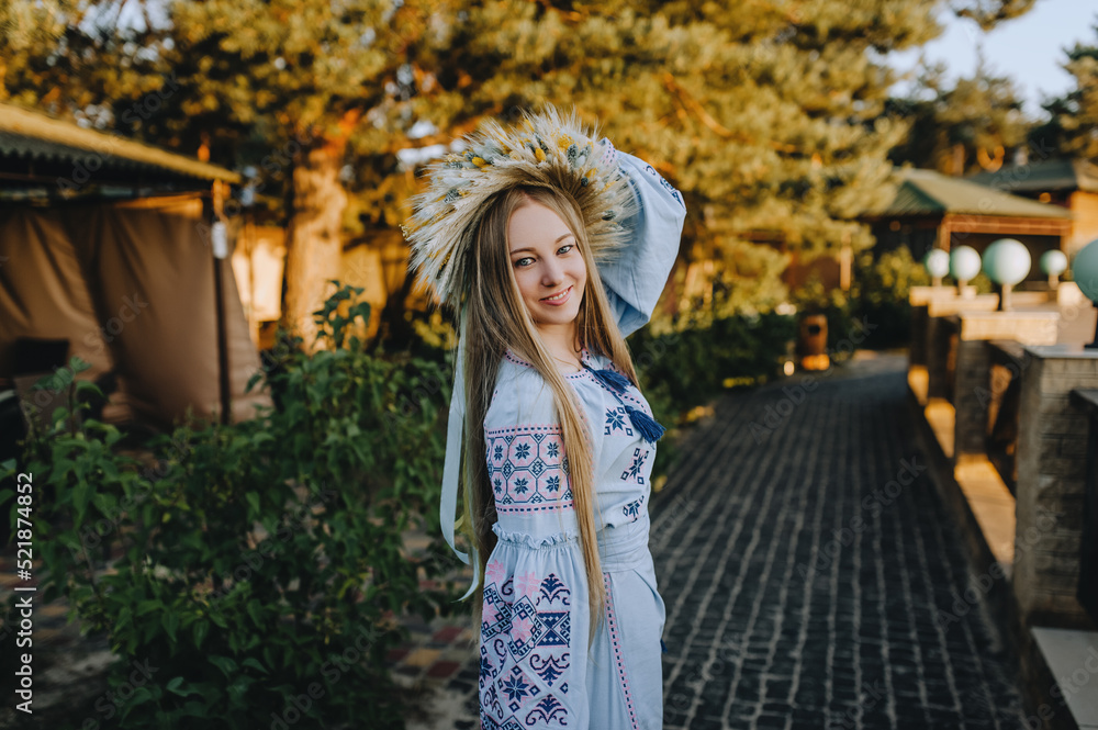 Portrait of a beautiful, young smiling Ukrainian girl in an embroidered, long dress with a wreath of wheat and wildflowers in the summer in a park in nature. Photography, Ukraine.