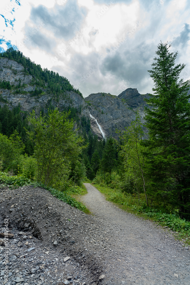 Fototapeta premium Wasserfall im Tal von Adelboden, weithin sichtbar über den Bäumen. Engstligenfälle am Talende. immer weniger Wasser kommt vom Gletscher auf der Engstligenalp den Wasserfall herunter
