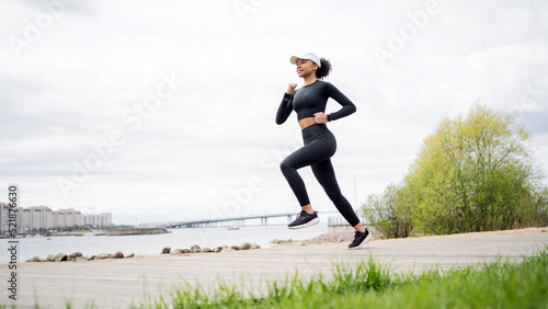 A female athlete runs does a workout on the street in sportswear and a fitness watch on her hand