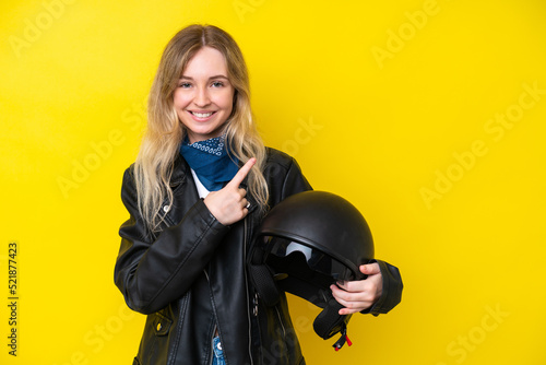 Blonde English young girl with a motorcycle helmet isolated on yellow background pointing to the side to present a product