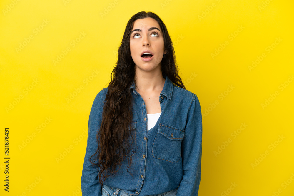 Young caucasian woman isolated on yellow background looking up and with surprised expression Young caucasian woman isolated on yellow background looking up and with surprised expression